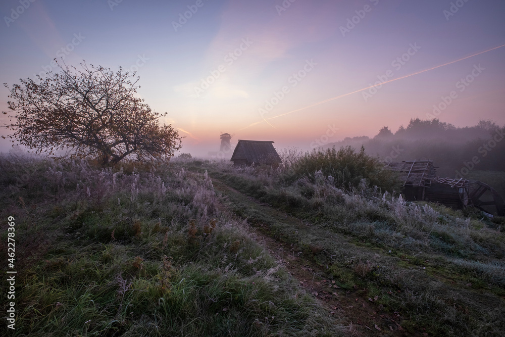 Traditional Russian countryside village with wooden windmill in autumn fog with first frosts at dawn