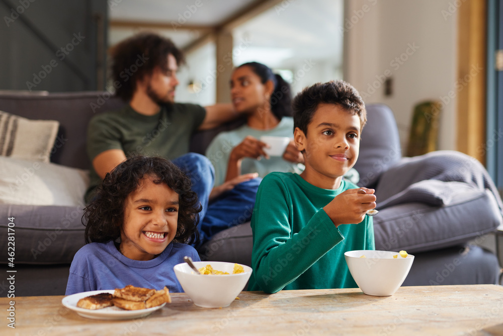 Children watching TV eating breakfast with parents