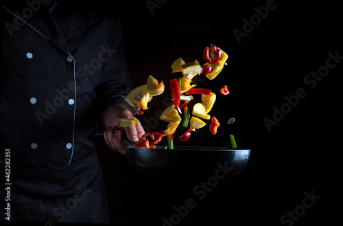 The chef prepares vegetables in frying pan. Cooking healthy vegetarian food and meal on a dark background. Free advertising space