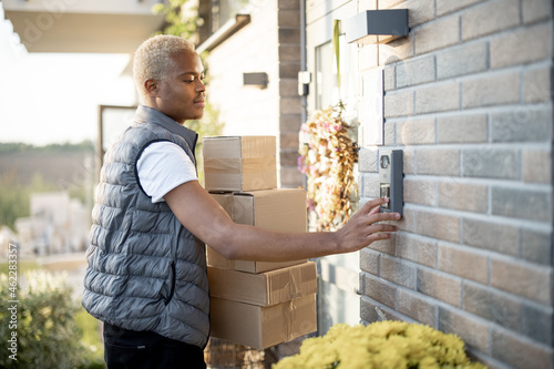 Slika na platnu Courier with parcels ringing in doorbell of client s house