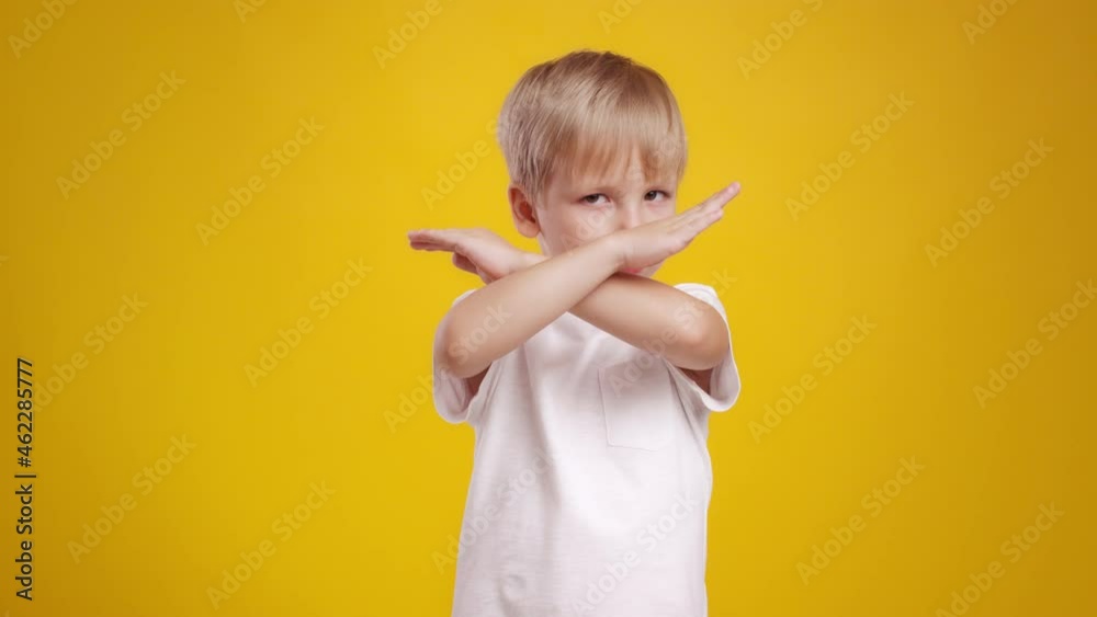 Cute little blonde boy showing stop gesture, crossing hands over orange studio background, slow motion Cute little blonde boy showing stop gesture, crossing hands over orange studio background, slow motion