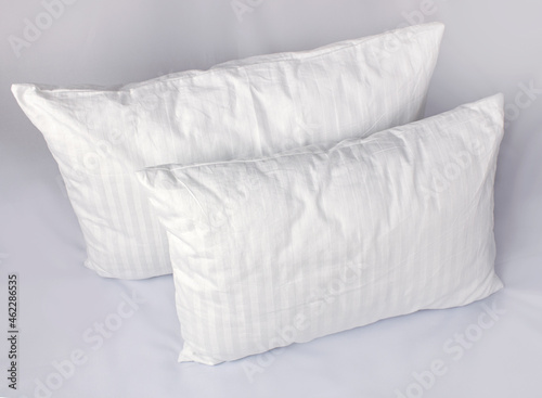 Fototapeta Naklejka Na Ścianę i Meble -  Two white pillows in striped cotton pillowcases. Satin jacquard bedding and accessories. Air soft pillows filled with swan down and bamboo