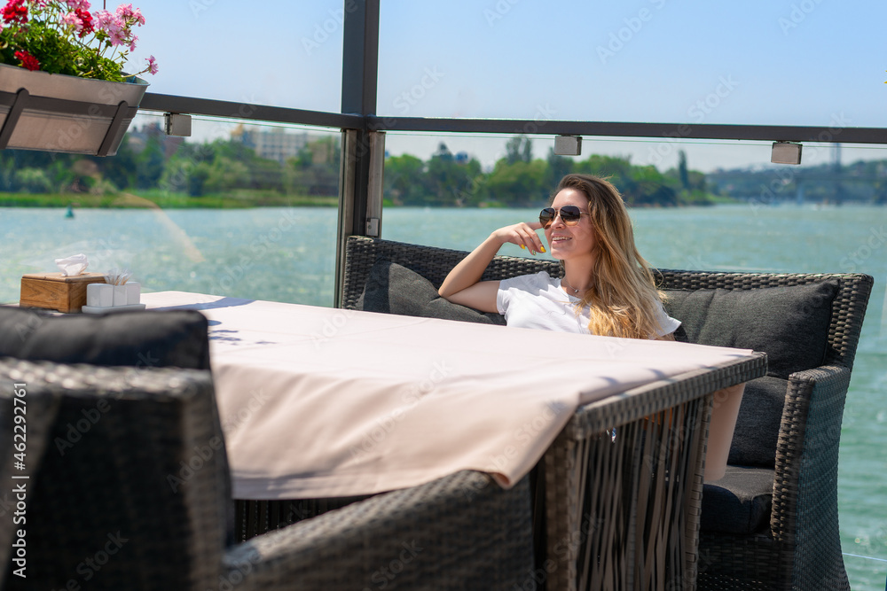 a girl in a cafe at a table by the sea looks into the distance with glasses
