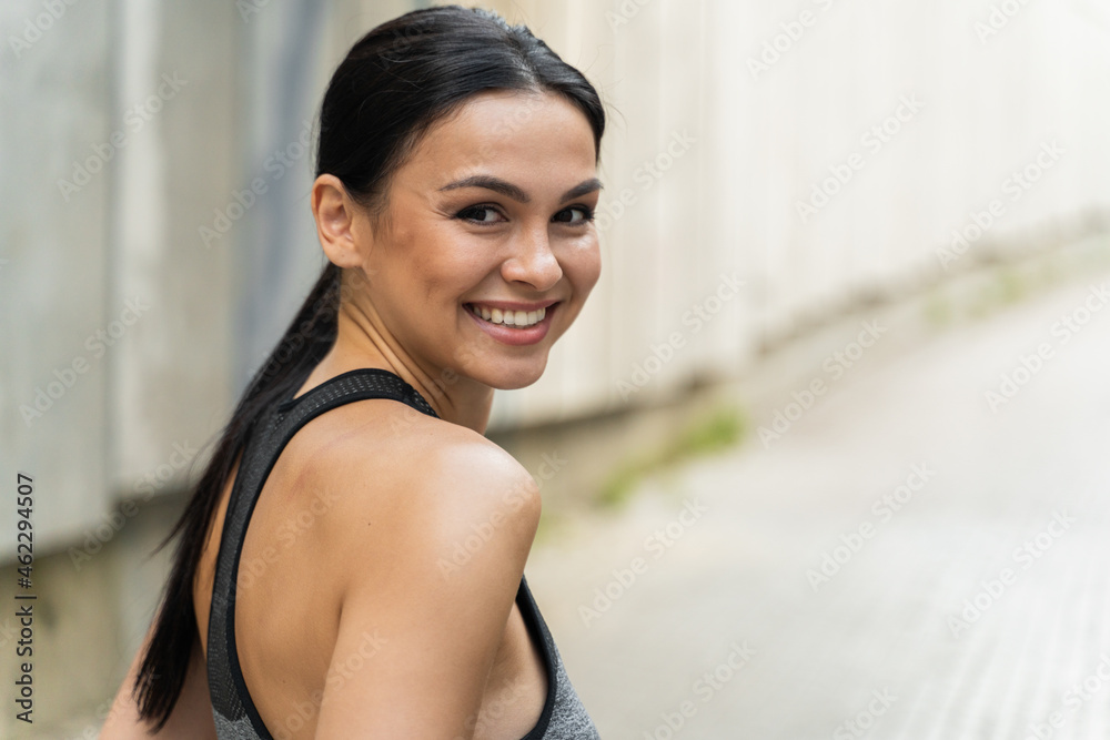 Portrait view of the brunette woman smiling to the camera while looking over her shoulder. Cheerful sportive girl feeling excited after training