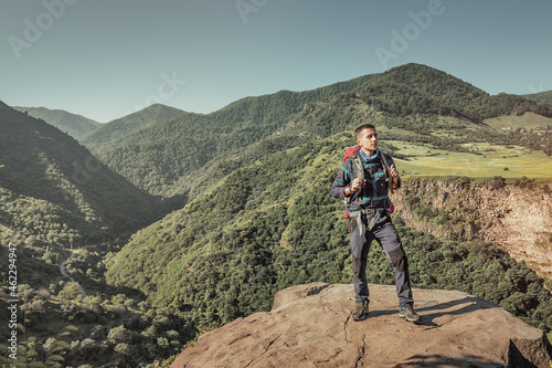 A male traveler with a trekking backpack climbs a rock in the mountains. Long distance trails and hike concept © EdNurg