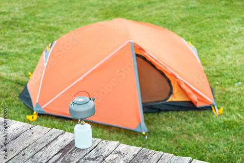 kettle on a gas burner with orange tent in a camping site. The stove is used for more eco-friendly and safe cooking instead of kindling a fire