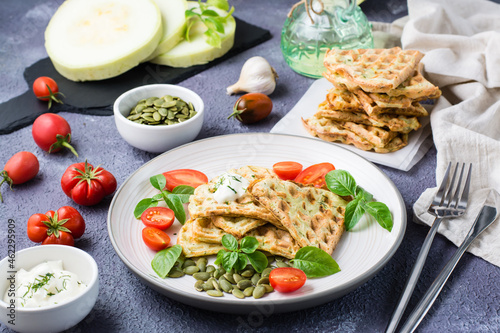 Ready-to-eat delicious zucchini waffles, tomatoes, basil and pumpkin seeds on a plate on the table. Vegetable diet food