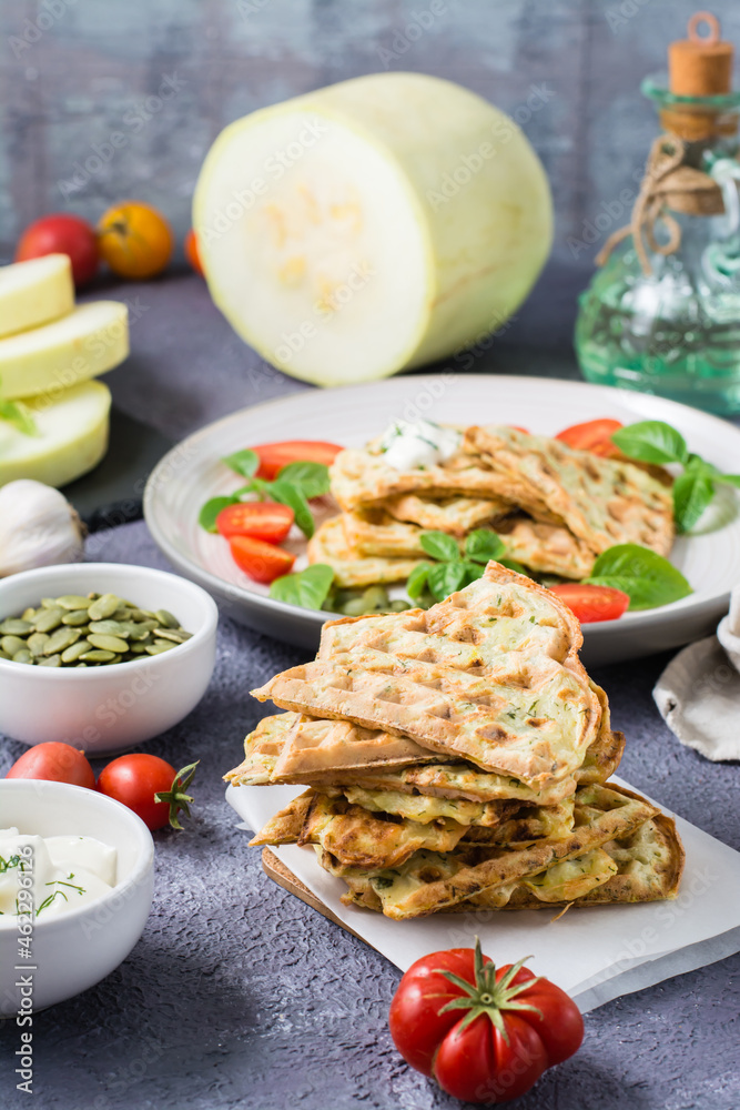 A stack of ready-to-eat zucchini waffles and basil on baking paper on the table. Vegetable dietary vegetarian food. Vertical view