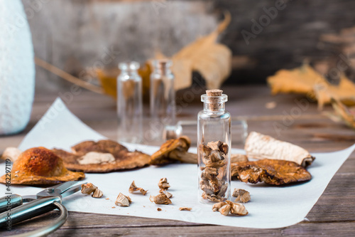 Dried chopped fly agarics stacked in a small jar and dry mushrooms on parchment on a wooden table. Microdosing and Alternative Medicine. photo