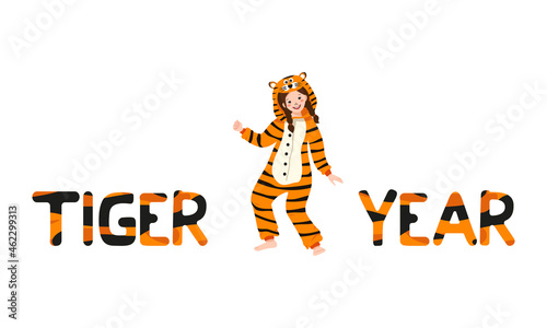Girl in tiger carnival costume and inscription New Year from striped orange with black letters. Children pajama party or holiday. Kid in jumpsuits or kigurumi, festive clothing for Christmas