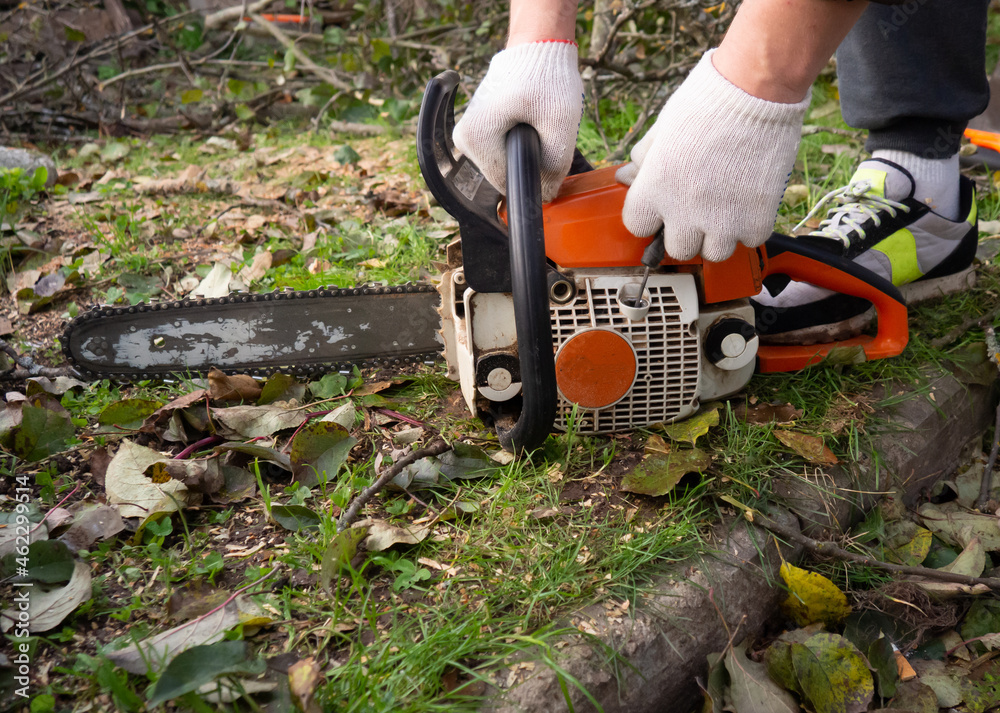 Naklejka premium a man's hands start a chainsaw in the garden