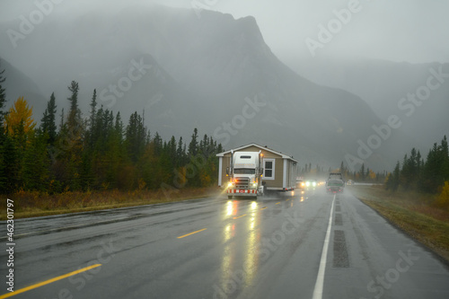 An oversize load truck carrying a prefabricated mobile home in extremely bad weather on a rainy day on a Canadian highway