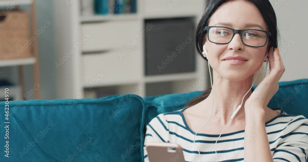 Beautiful happy caucasian woman with glasses sitting at home on couch and listening to music on headphones enjoying good sound. Beautiful happy caucasian woman with glasses sitting at home on couch and listening to music on headphones enjoying good sound.