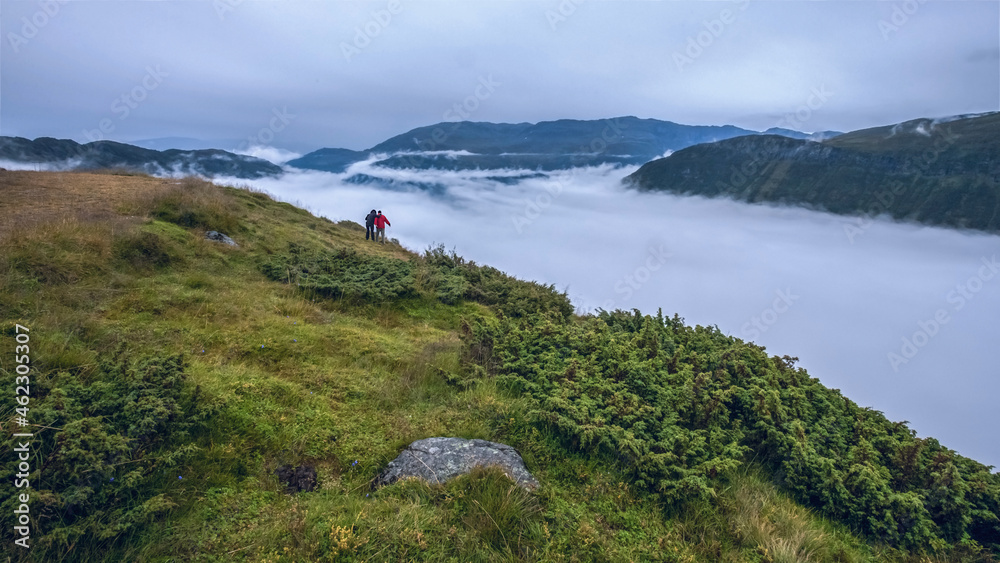 Hikers on the cliff above the clouds travel, hiking in the mountains adventure extreme summer travel outdoor vacation in Norway.