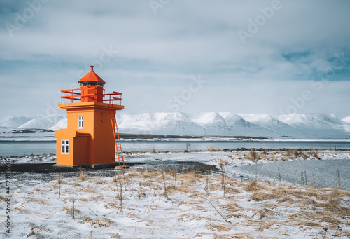 Beautiful view of orange colored lighthouse on the northcoast of Iceland, west Iceland in winter season with volcanic rocks and brown grass on cloudy day. photo