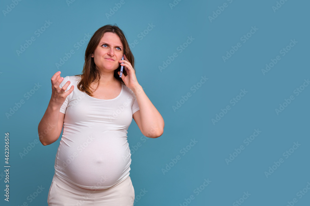 Portrait of a pregnant woman talking angrily on the phone on a blue background Portrait of a pregnant woman talking angrily on the phone on a blue background