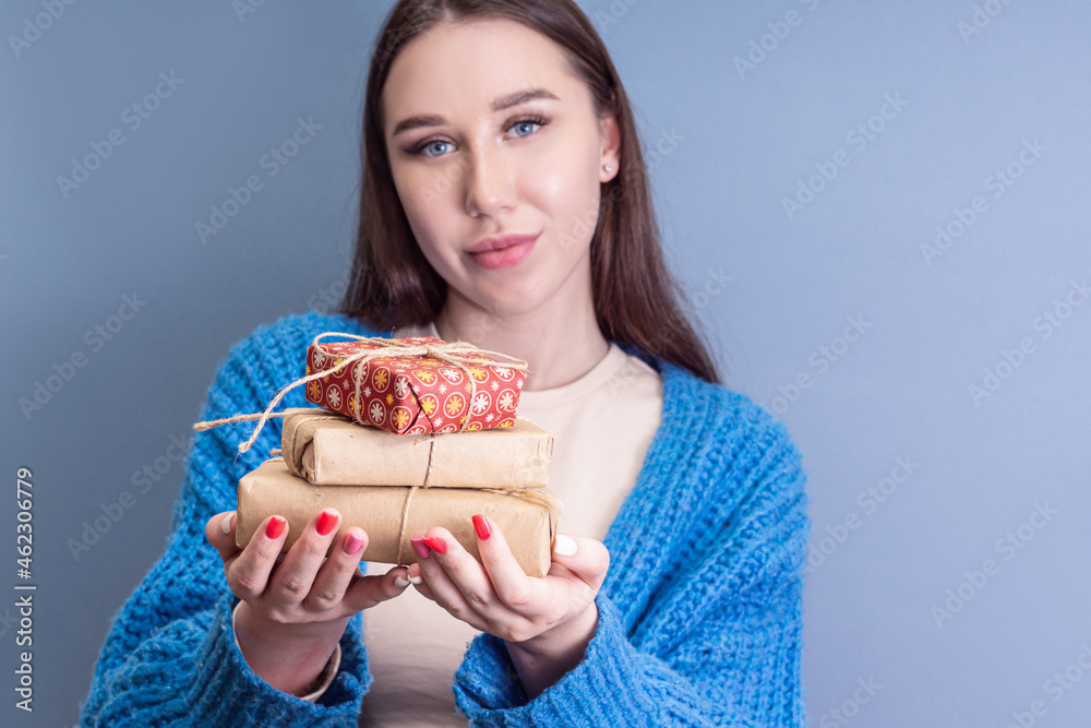 Woman holds stack of Christmas gifts on blue background