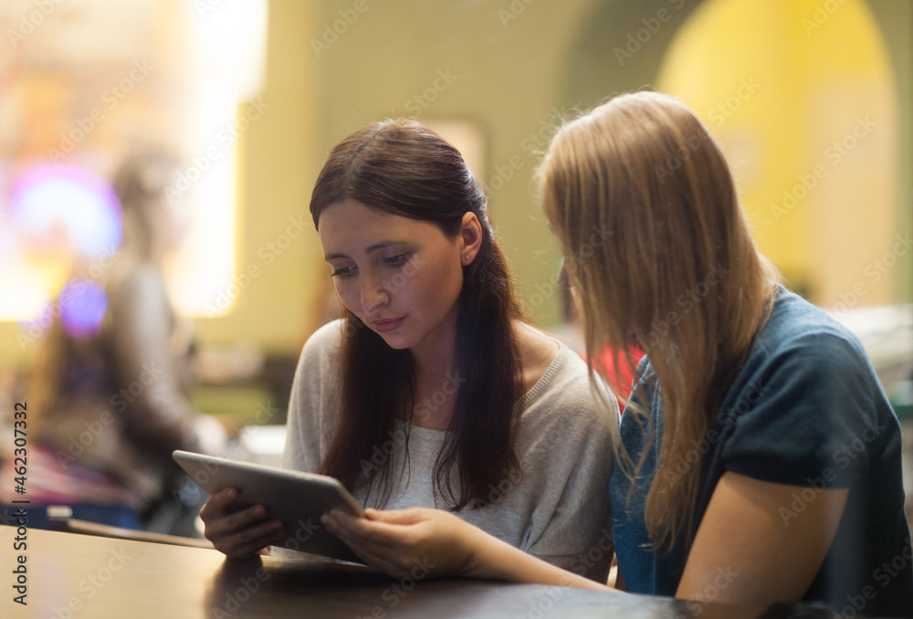 Two women in the restaurant using electronic tablet Two women in the restaurant using electronic tablet