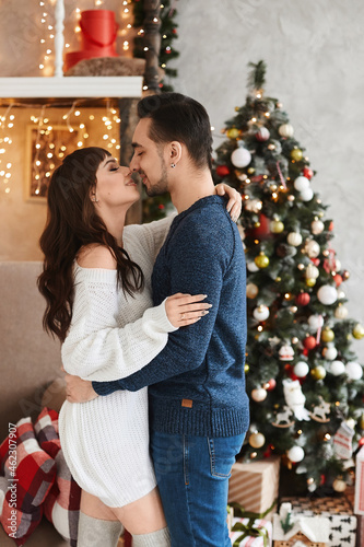 Young sweet heterosexual couple posing in the living room interior decorated for New year holidays