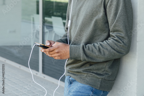 Close up view of a man using his mobile phone with earphones while standing outdoors on the street. Urban concept. © MANUEL