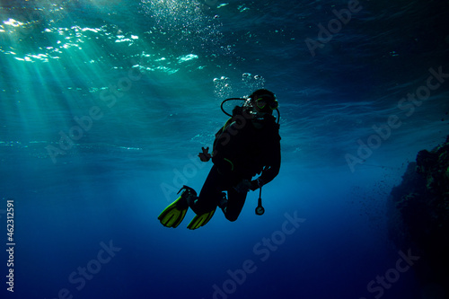 Woman scuba diver swimming in deep blue with sun rays
