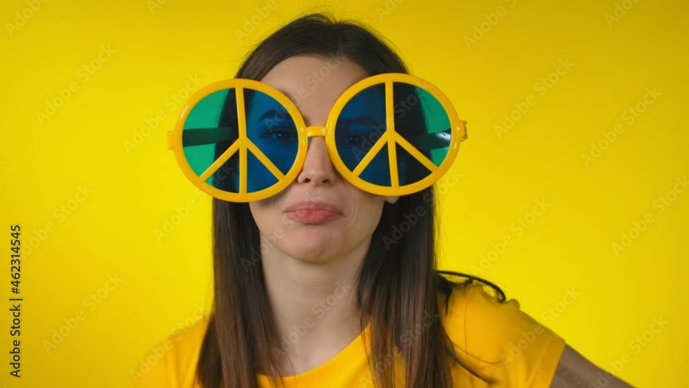 Cheerful woman in funny yellow hippie sunglasses is posing on yellow background