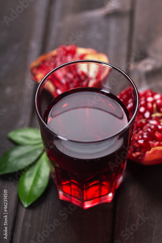 Glass of pomegranate juice with pieces ans leaves of pomegranate fruits on a dark wooden table