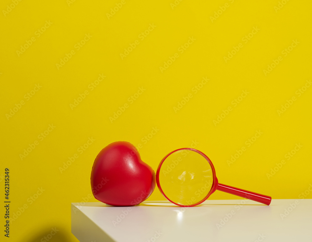red plastic heart and magnifier on a white table. Finding a donor organ red plastic heart and magnifier on a white table. Finding a donor organ