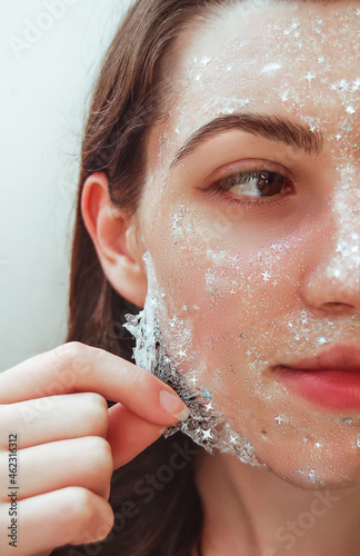 Beautiful young woman with healthy skin removes purifying transparent peel off mask with shiny sparkling star glitter from her face. Trendy cosmetic beauty procedure.Skin care concept.