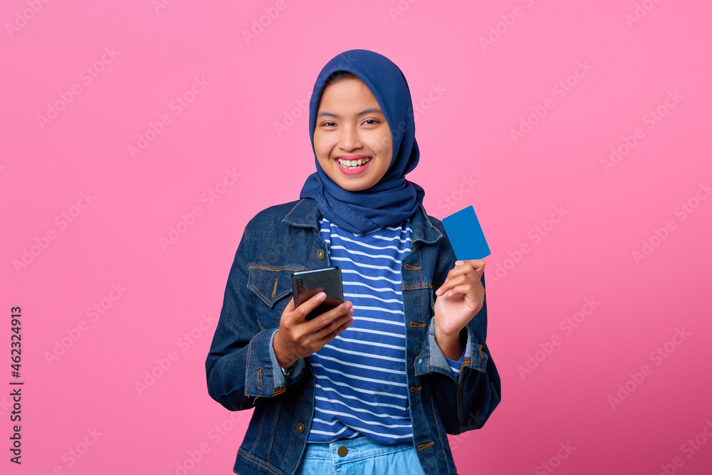 Portrait of smiling young Asian woman holding smartphone while showing credit card Portrait of smiling young Asian woman holding smartphone while showing credit card