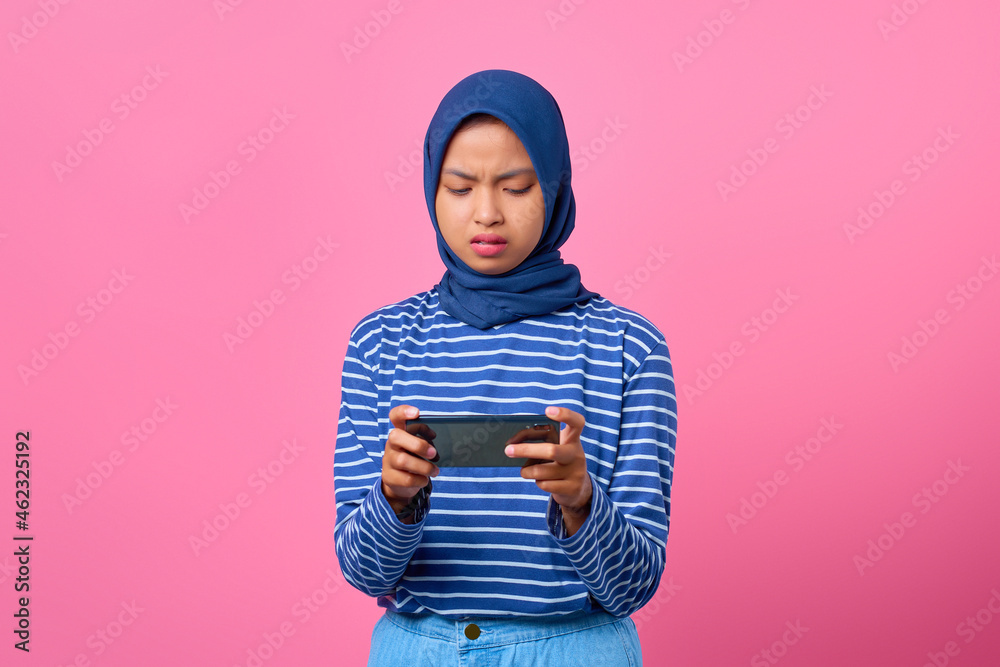 Portrait of disappointed young Asian woman playing video game on mobile phone