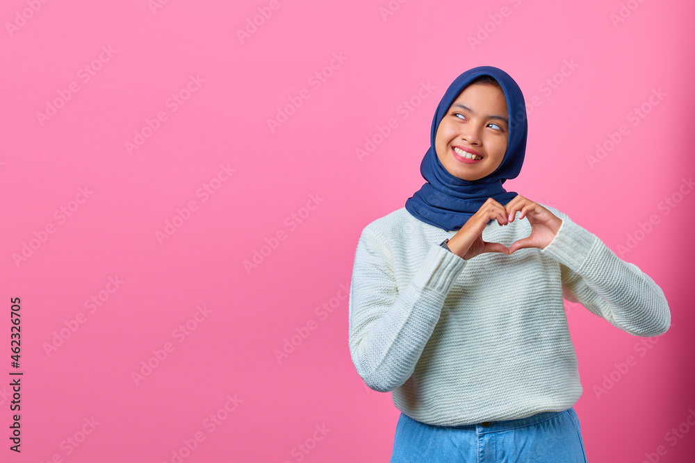 Obraz premium Portrait of smiling young Asian woman showing heart shape gesture with two hands