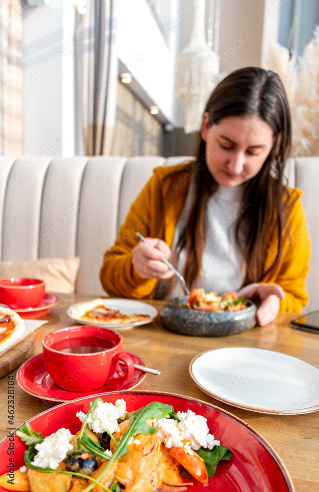 Young woman in orange cardigan is having lunch of healthy vegetarian salad bowl and slice of pizza.