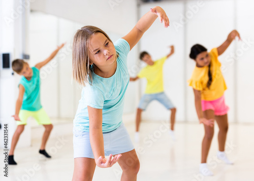 Young girl and her friends performing modern dance in studio during rehearsal.