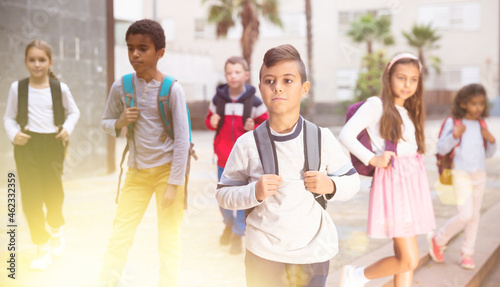 Portrait of positive boy standing near school, children on background