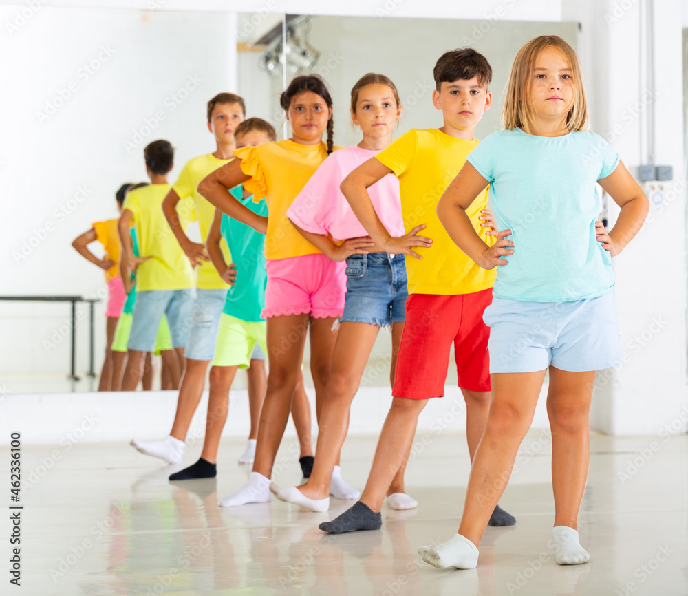 Group of focused tween children standing akimbo in row one by one, learning movements of folk dance in choreography lesson