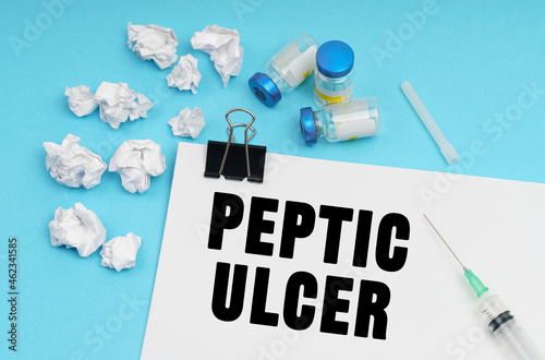On a blue background, a syringe, medicine, crumpled pieces of paper and a sheet with the inscription - Peptic ulcer