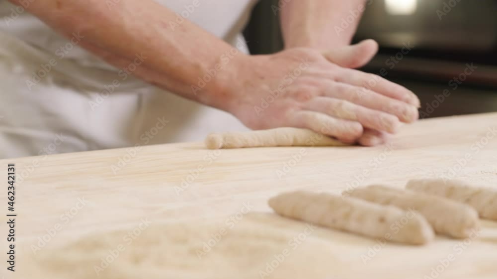 European senior baker rolling raw dough on wooden desk, bakery chef rolling out dough for bread rolls European senior baker rolling raw dough on wooden desk, bakery chef rolling out dough for bread rolls