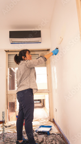 Young latin woman painting a wall in her apartment