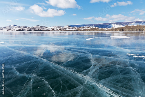 Beautiful winter landscape of frozen Baikal Lake on a sunny February day. Blue smooth ice with cracks in the Small Sea Strait. Ice travel in winter holidays. Natural background