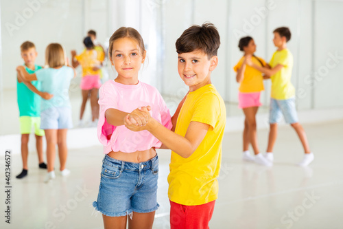 Interested modern tween boy and girl practicing slow pair dancing during group class in dance studio for children.