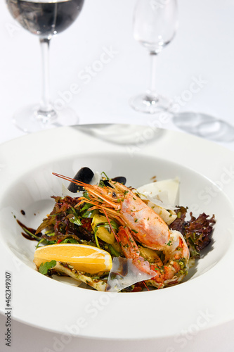 Fresh healthy salad with shrimp, mussels, rucola, lettuce and vegetables. Elegant contemporary appetizers with seafood on white table with wine glass. Still life - Lunch in seafood restaurant.