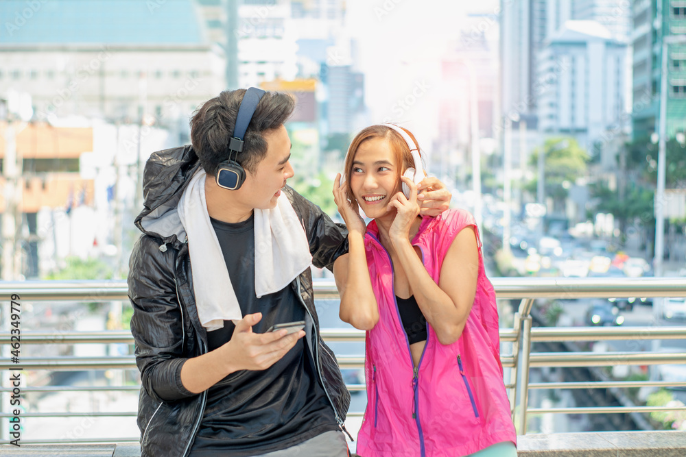 Young Asian couples enjoying outdoor exercise and relaxation, happiness with mobile phones and headphones to listen to music and ,check health with smart artificial intelligence technology