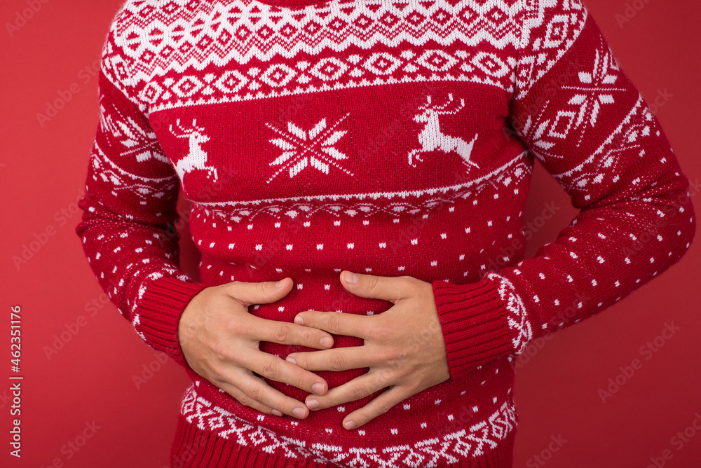 Cropped closeup photo of man in red and white christmas sweater holding his hurting stomach on isolated red background