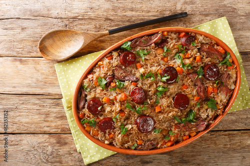Authentic Arroz de pato duck rice is a traditional recipe from Portugal cooked with red wine, onion, carrot and chorizo close up in the baking dish on the wooden table. Horizontal top view from above