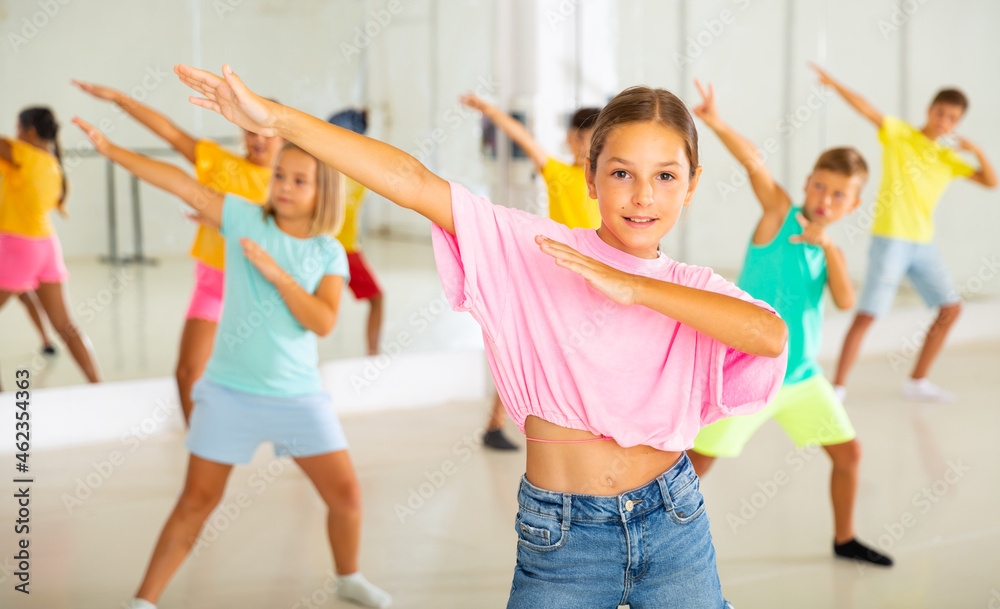 Fototapeta premium Positive girl exercising in group of classmates during dance class at school