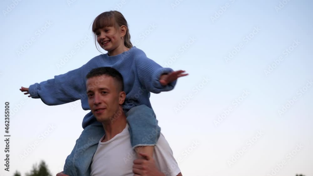 The little daughter is sitting on her dad's neck. Carefree dad and daughter go out on the weekend. Happy healthy family The little daughter is sitting on her dad's neck. Carefree dad and daughter go out on the weekend. Happy healthy family