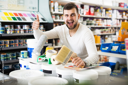 Happy young man buying tools for house decoration in paint supplies store