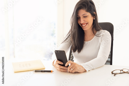 Young smiling businesswoman using a smartphone near a computer in the office