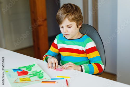 Little kid boy making paper origami tulip flowers for a postcard for mother's day or birthday. Cute child of elementary class school doing handicraft